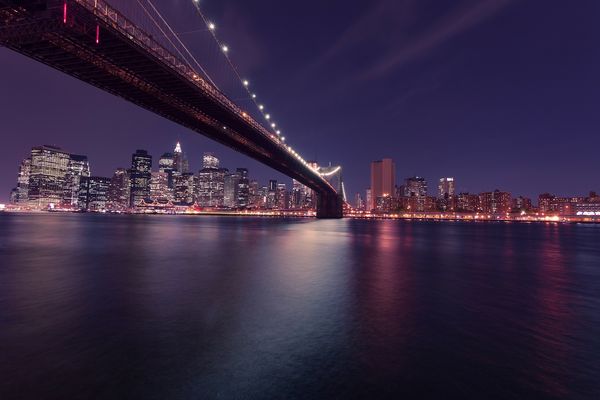 Zdjęcie przedstawia most w nocy na tle panoramy Nowego Jorku