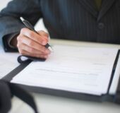 obrazek dekoracyjny przedstawiający rękę osoby, która podpisuje dokumenty