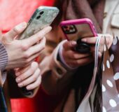 Na zdjęciu znajdują się dwie osoby z telefonami w rękach. Nie widać twarzy osób, jedynie tułów i dłonie