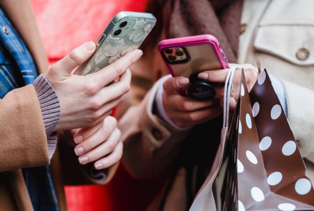 Na zdjęciu znajdują się dwie osoby z telefonami w rękach. Nie widać twarzy osób, jedynie tułów i dłonie