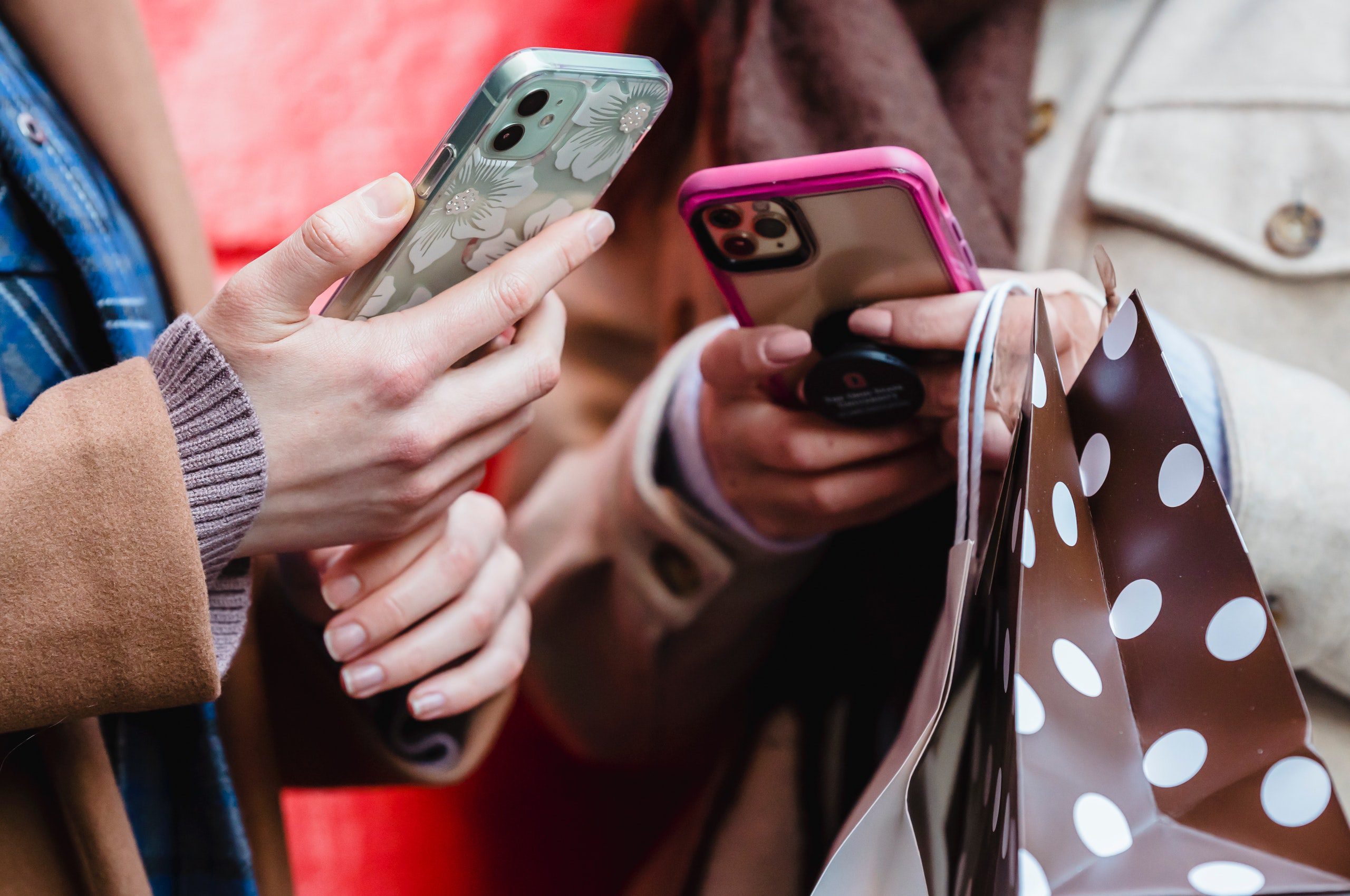 Na zdjęciu znajdują się dwie osoby z telefonami w rękach. Nie widać twarzy osób, jedynie tułów i dłonie