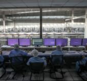 Obrazek przedstawiający grupę ludzi przed ekranami, ubrani są w stroje laboratoryjne