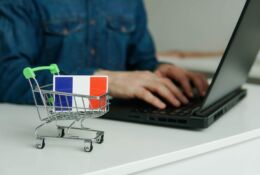 Mężczyzna pracuje na laptopie, obok znajduje się wózek na zakupy z flagą Francji