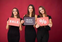 Three young women holding placards with the words Sale, Black Friday, %.