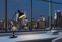 lampka biurkowa na tle okna z ktorego jest widok na wielkie nowoczesne miasto