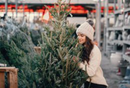 Elegant girl buys a Christmas tree. Woman in a white knited sweater. Beautiful lady with dark hair.