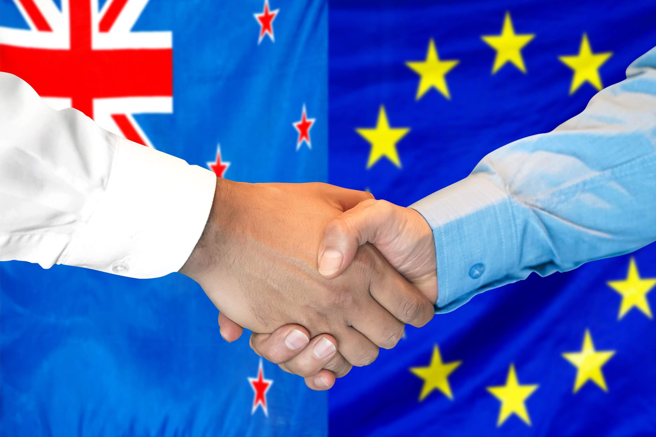 Uścisk dłoni na tle flag UE i Nowej Zelandii