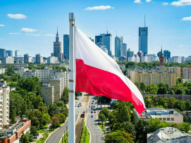 Polish national flag against skyscrapers in Warsaw city center, aerial landscape under blue sky