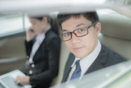 wnetrze samochodu z dwojgiem Japonczykow, mężczyzna wygląda przez okno a kobieta rozmawia przez telefon