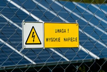 A warning sign mounted on the fence of a solar farm