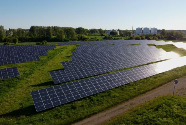 Instalacje fotowoltaiczne na zielonym polu, słoneczna pogoda, promienie słońca odbijają się od paneli słonecznych