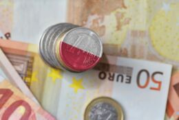 Moneta euro z efektem biało-czerwonych barw położona na tle banknotów euro o różnych nominałach