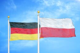 Flagi Polski i Niemiec powiewają na tle błękitnego nieba