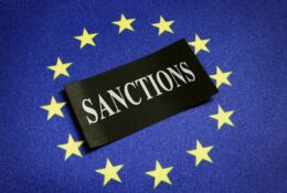 Symbol UE, w środku czarna etykieta z białym napisem SANCTIONS (sankcje)