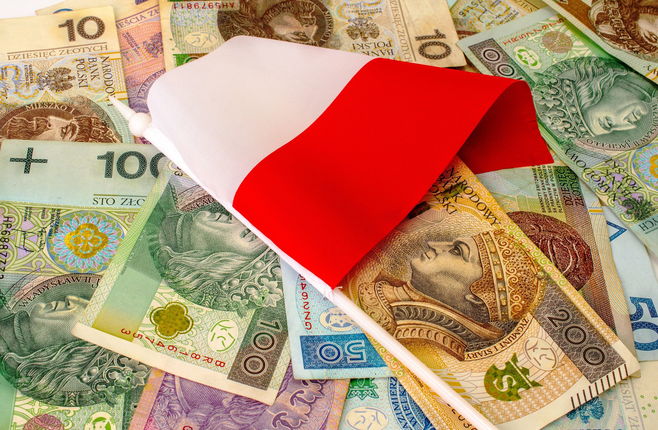 Wiele banknotów PLN o różnym nominale. Mała flaga Polski