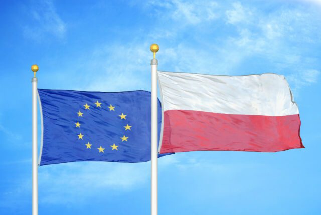 Powiewające na wietrze flagi Polski i Unii Europejskiej na tle nieba