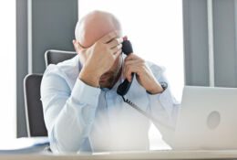 Biały mężczyzna w średnim wieku rozmawia przez telefon, opierając głowę na ręku