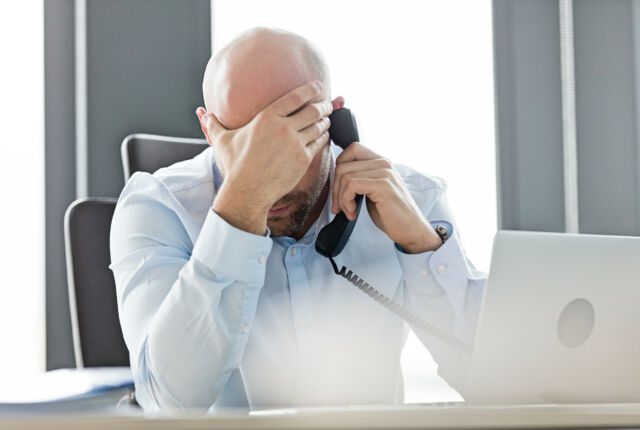 Biały mężczyzna w średnim wieku rozmawia przez telefon, opierając głowę na ręku