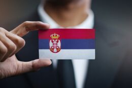 mężczyzna w garniturze trzymający w dłoni mini flagę Serbii