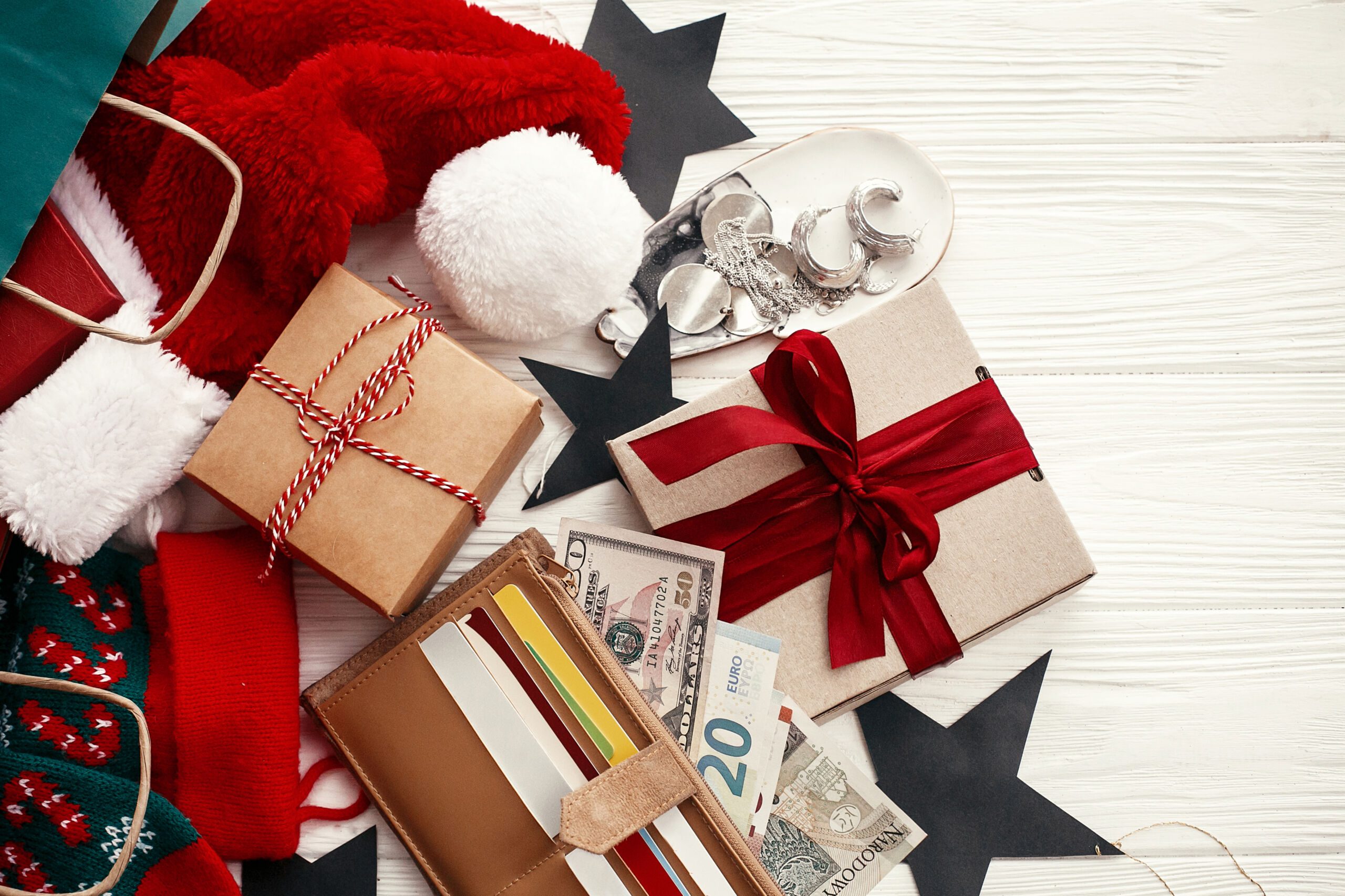 Koncepcja świątecznych zakupów i wyprzedaży. Karty kredytowe i pieniądze w portfelu, papierowe torby z ubraniami, pończochy, pudełka na prezenty i biżuteria na białym, rustykalnym tle.
