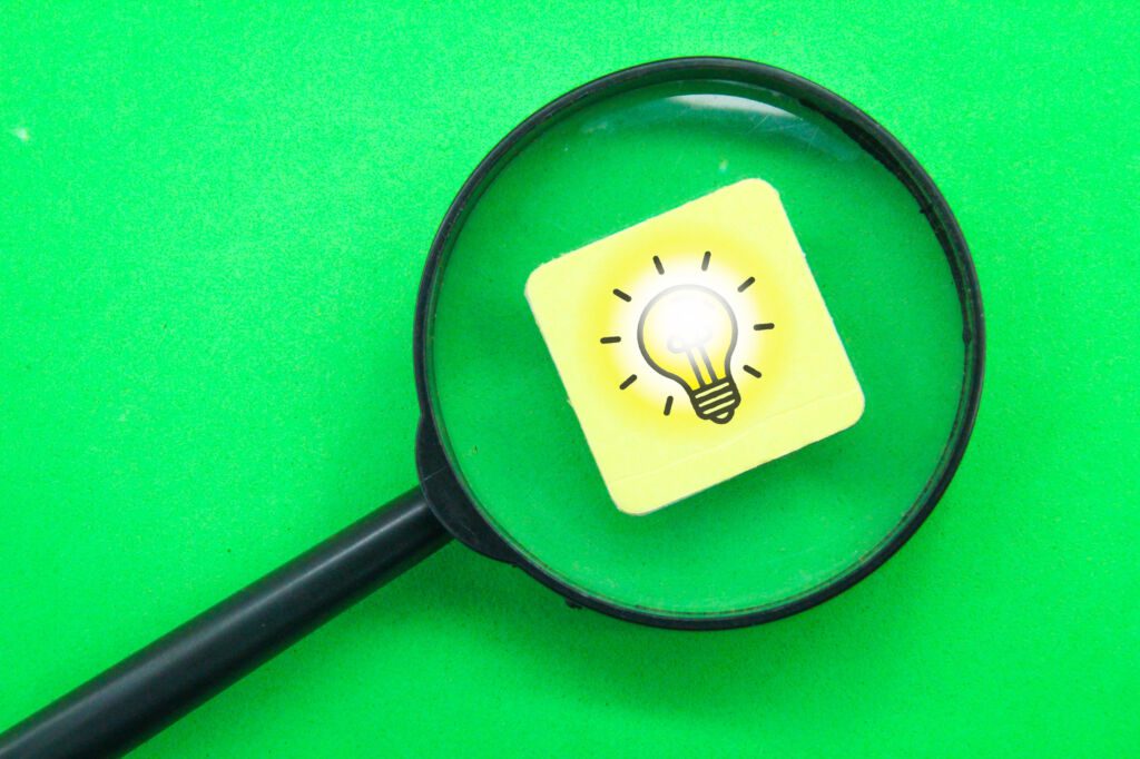 Szkło powiększające skierowane na klocek z żarówką na zielonym tle.