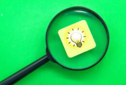 Szkło powiększające skierowane na klocek z żarówką na zielonym tle.